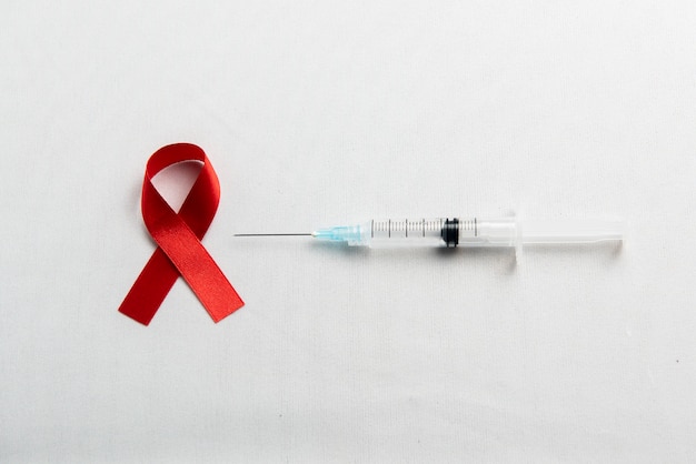 Free Photo red ribbon and syringe with white background. hiv aids ribbon awareness