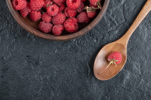 red ripe raspberries in wooden bowl on marble table