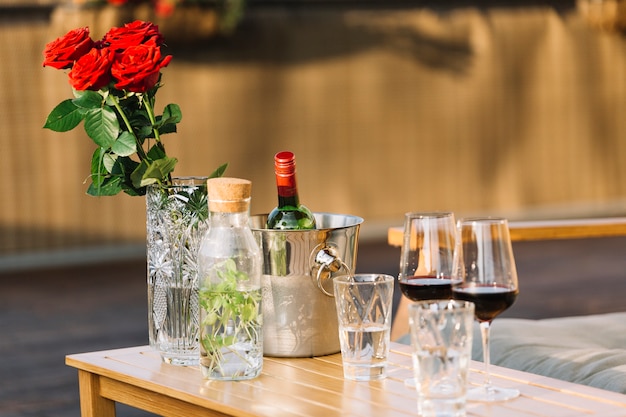 Red roses vase; ice bucket and wine glasses on wooden table