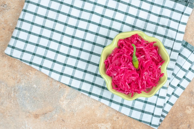 Red sauerkraut salad in green bowl with tablecloth.