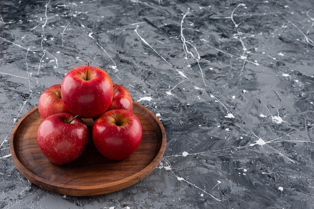 Free photo red shiny whole apples placed on wooden plate.