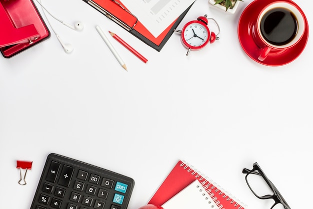 Red stationeries,alarm clock,and calculator on white desk