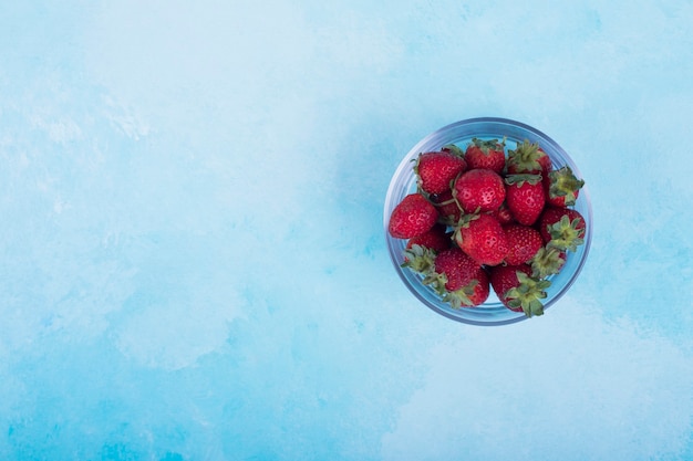 Red strawberries in a glass cup on blue on the right.