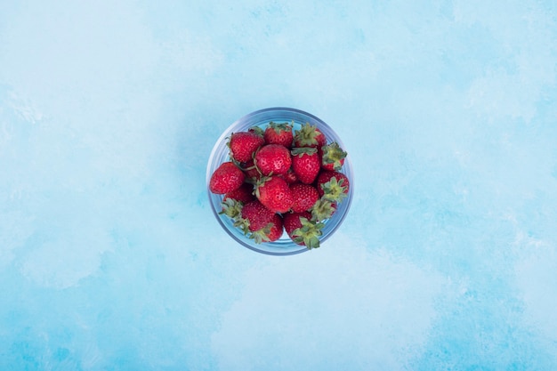 Red strawberries in a glass cup on blue