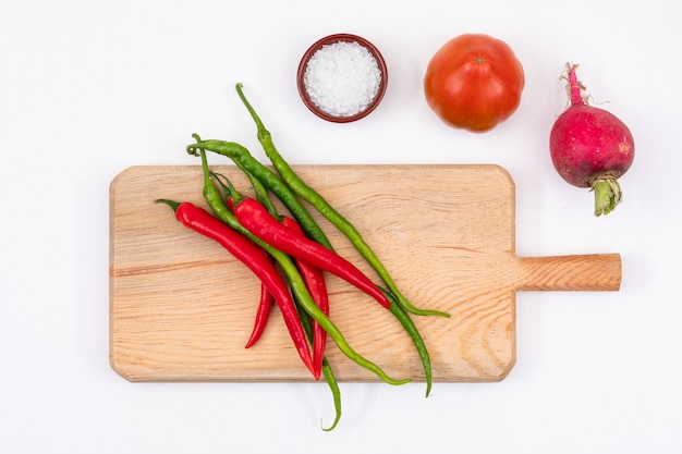 Red tomato, radish, red and green chili peppers with wooden cutting board