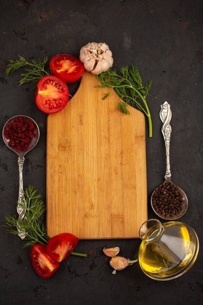 Red tomatoes along with greens garlic slices and oil surrounded by yellow wooden desk