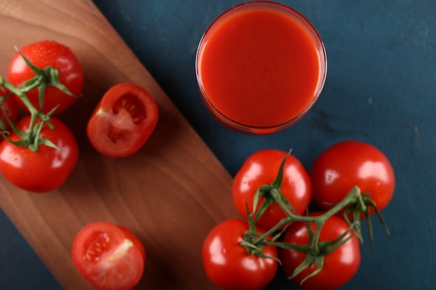 Red tomatoes and a glass of juice on a wooden board. Top view.