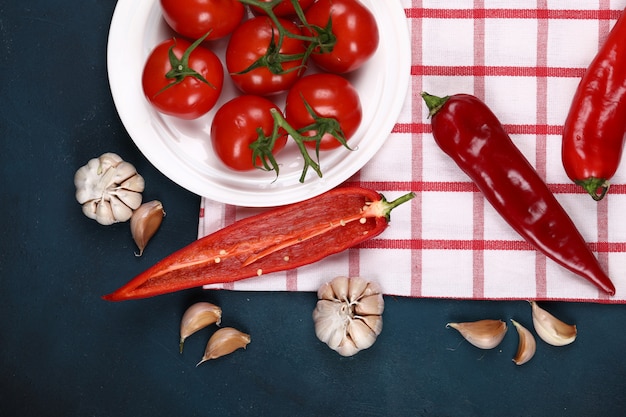 Red tomatoes in a white plate on a checked towel with chilies and garlics.