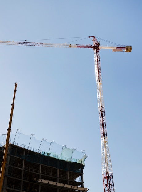 Free Photo red and white construction crane in front of building against blue sky