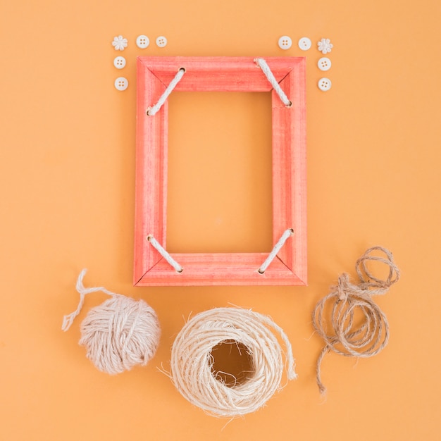 Free photo red wooden frame decorated with button and different spools on an orange backdrop