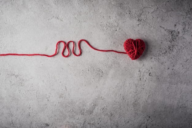 Free photo red yarn heart shaped on the wall background