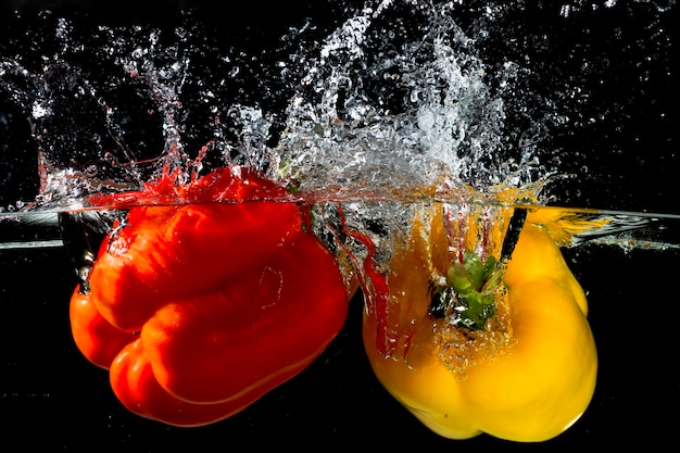 Red and yellow bell pepper splash into clear water