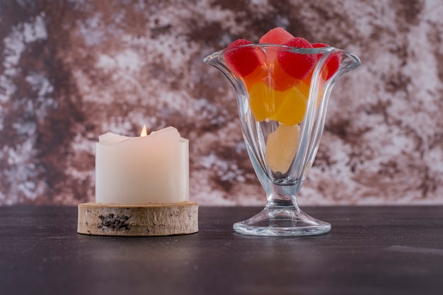 Red and yellow marmelades in a glass cup with a candle aside on marble space