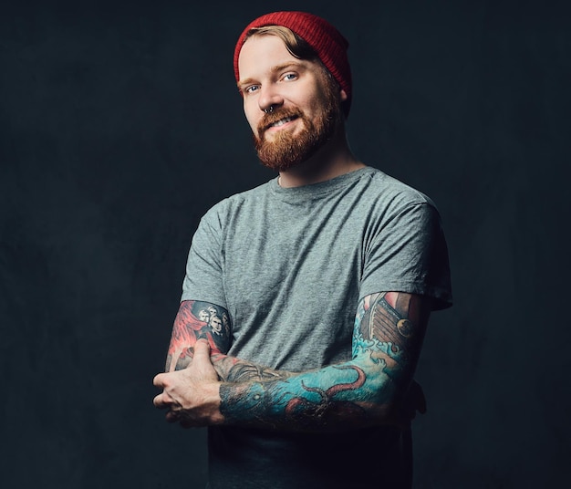 Redhead bearded male with tattoos on his arms posing over grey background.