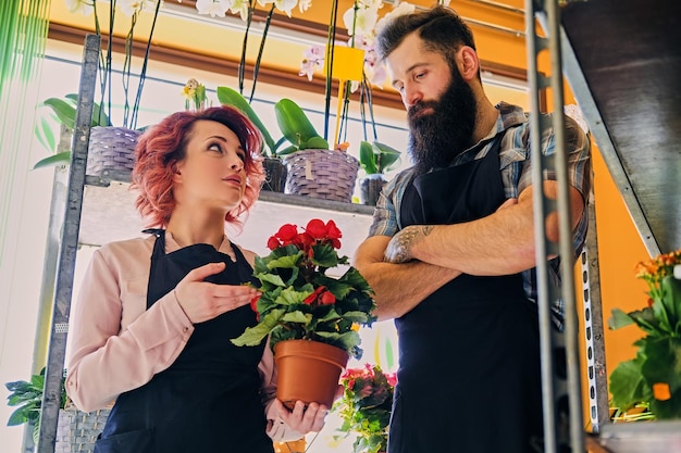 Free photo redhead female and bearded tattooed male selling flowers in a market shop.