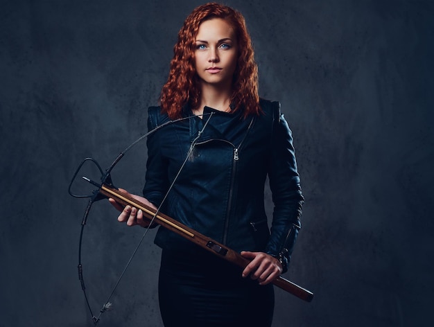 Free Photo redhead female dressed in an elegant suit holds crossbow.