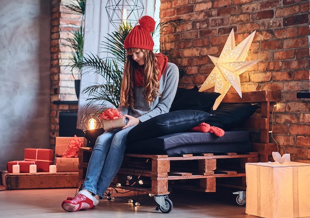 Free photo redhead female holds a christmas gift in a living room with loft interior.