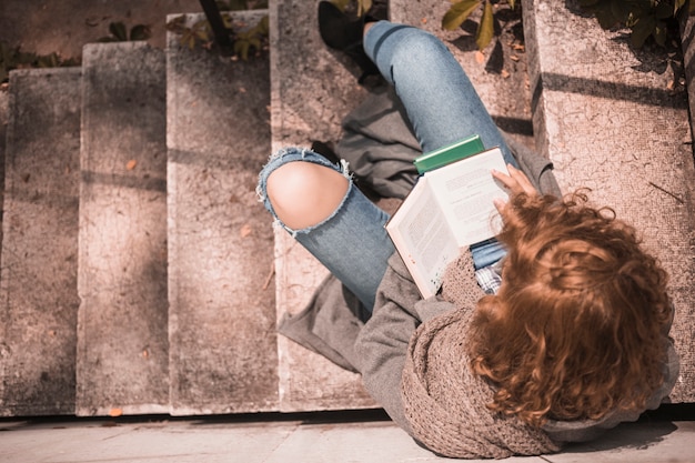 Free photo redhead female with opened book on stone stair