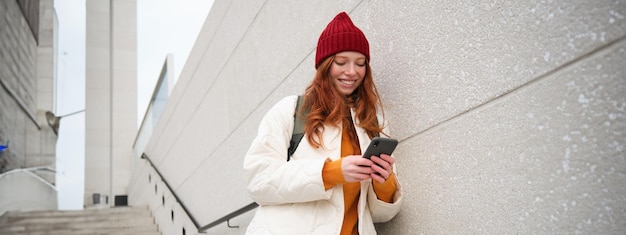 Free Photo redhead girl young woman tourist with backpack holds smartphone looks for route on mobile