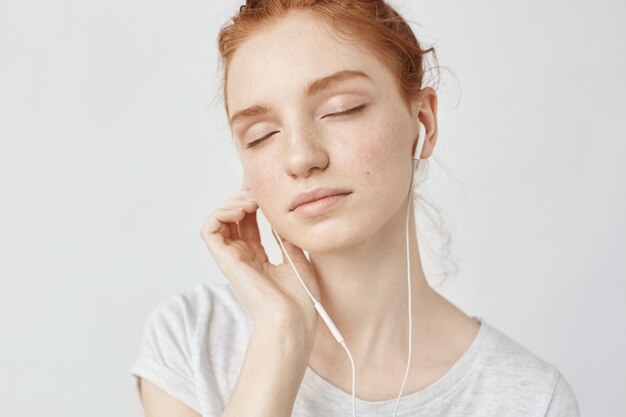 Redhead woman listening music in headphones with closed eyes.