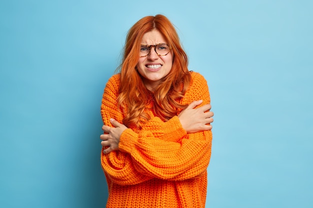 Free photo redhead woman trembles from cold hugs herself to warm up walks outdoor during freezing temperature clenches teeth and shakes wears only sweater.