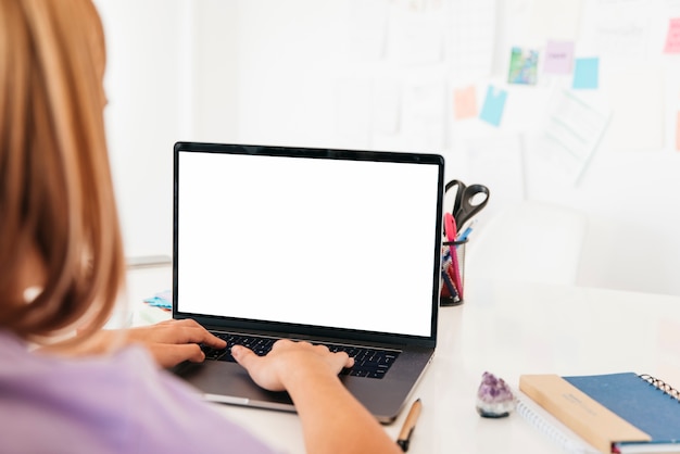 Redhead woman typing on laptop at desk near wall with notes