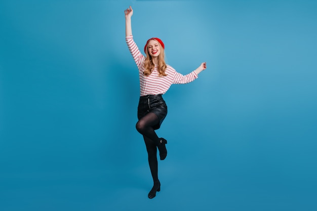 Free photo refined blonde girl dancing and waving hands.  magnificent french woman posing on blue wall.