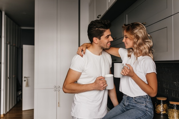 Refined girl drinking coffee with husband. Relaxed couple chilling in kitchen in morning.