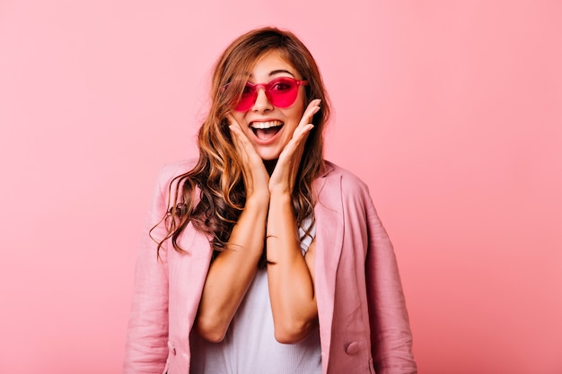 Refined white lady posing with surprised smile on rosy. Gorgeous long-haired girl in funny pink glasses fooling around.