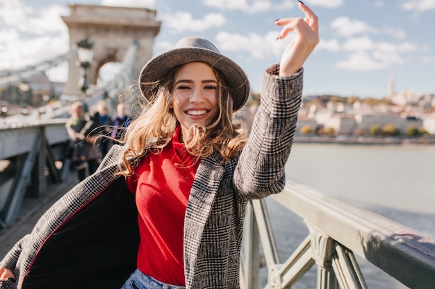 Free photo refined woman in trendy gray coat having fun during photoshoot on bridge