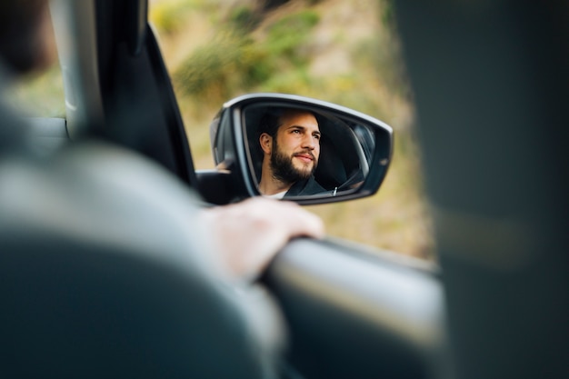 Free photo reflection of happy male in side mirror of car