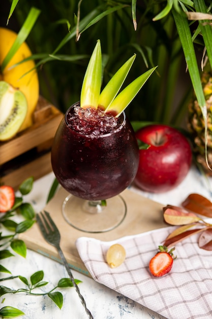 Refreshing summer alcoholic cocktail margarita with crushed ice and citrus fruits inside glass with strawberries and apple on kitchen table 