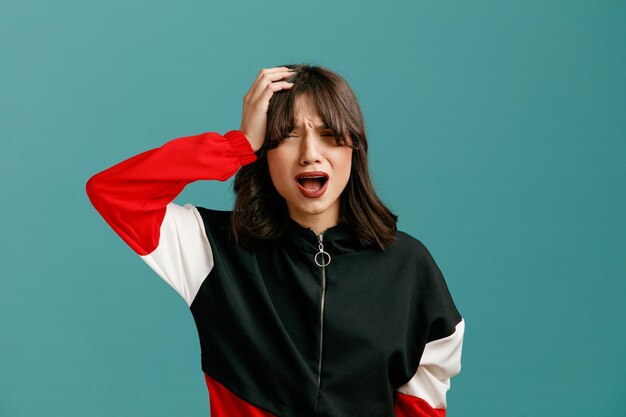 regretful young caucasian woman keeping hand on head looking at camera isolated on blue background