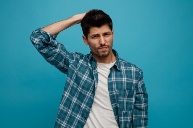 Regretful young man keeping hand on head looking at camera isolated on blue background