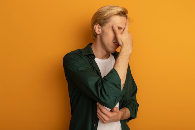 Free Photo regretted young blonde guy wearing green t-shirt covered face with hand