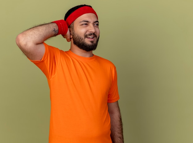 Free Photo regretted young sporty man looking at side wearing headband and wristband putting hand