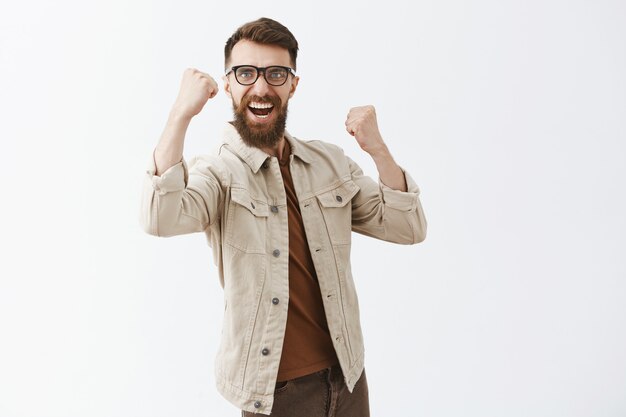 Rejoicing bearded man in glasses posing against the white wall