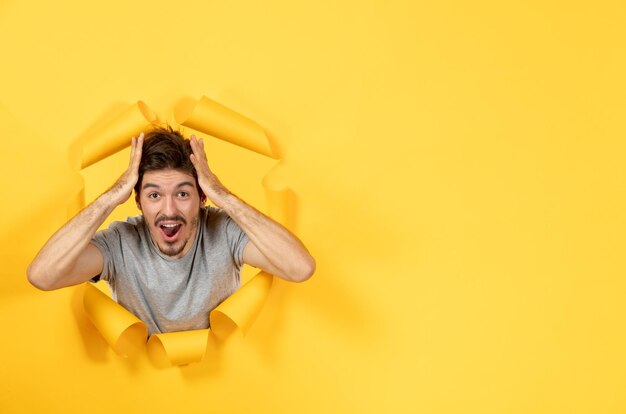 Rejoicing young male looking from torn yellow paper surface