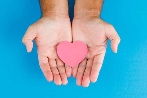 Relationship concept on blue table flat lay. hands holding paper cut heart.