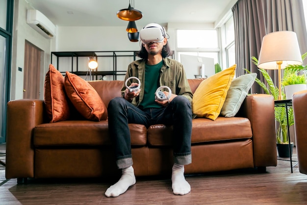 Free photo relax casual asian adult man wearing virtual reality headset and holding controllers plays in a sport video game at home playing vr active sport game online in the living room