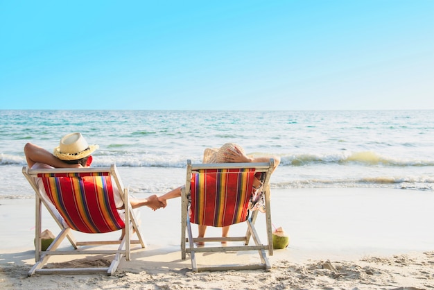 Relax couple lay down on beach chiar with sea wave - man and woman have vacation at sea nature concept