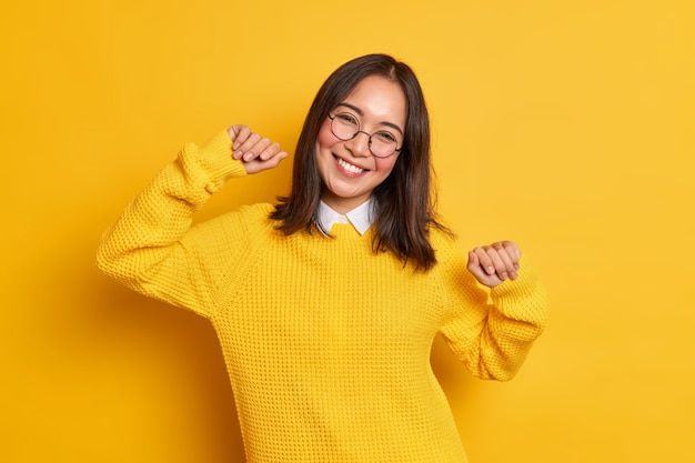 Free photo relaxed brunette pretty woman with eastern appearance raises arms and smiles pleasantly tilts head has positive face expression wears warm jumper.