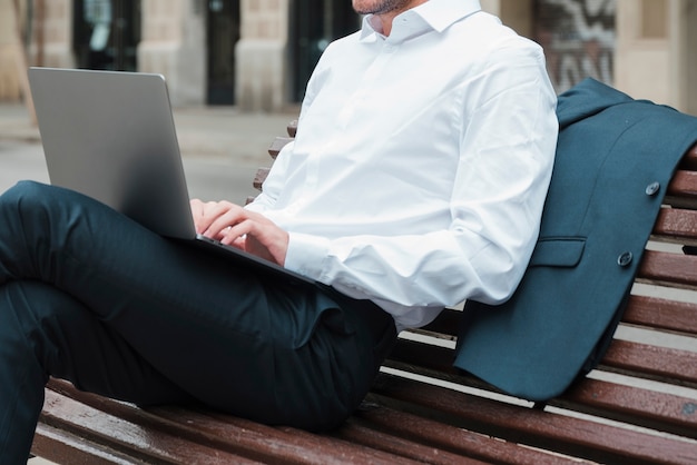 Relaxed businessman sitting on bench using laptop