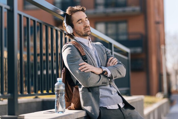 Relaxed businessman with eyes closed listening music over headphones on the street