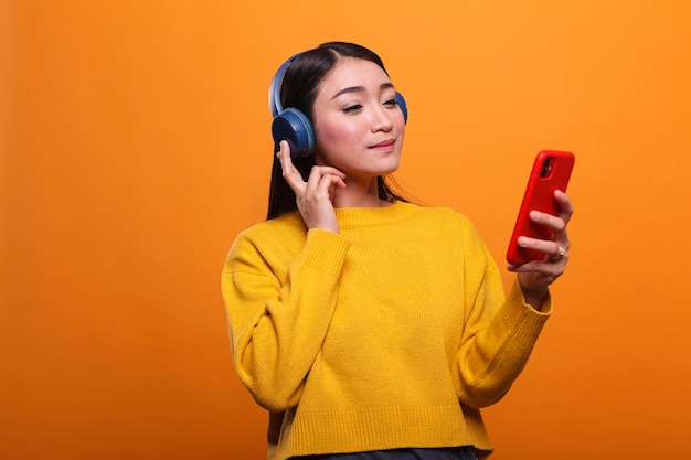 Free Photo relaxed friendly cute asian woman listening to music on audio streaming platform while using smartphone device. calm person wearing headphones while enjoying leisure time by listening to song.