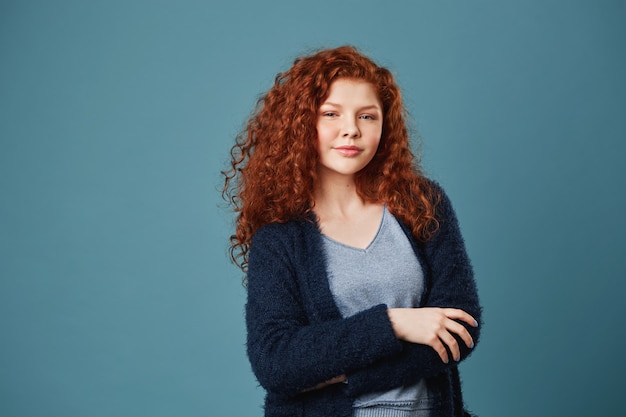 Free Photo relaxed handsome woman with ginger wavy hair and freckles holding hands crossed in front of her, looking with confident expression.