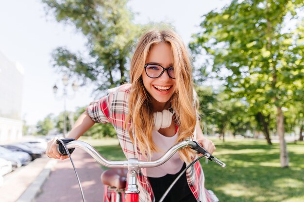 Free photo relaxed long-haired girl in headphones riding on bike. magnificent lady with cute smile sitting on bicycle.