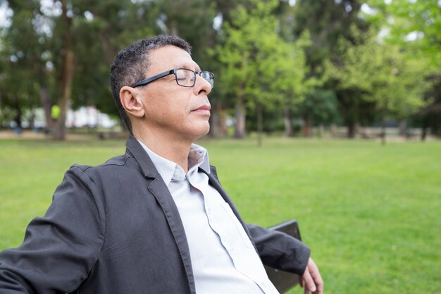 Relaxed middle-aged man sitting on bench in park