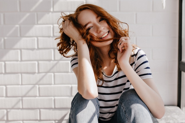 Free photo relaxed well-dressed girl sitting. stunning caucasian woman playing with her ginger hair.