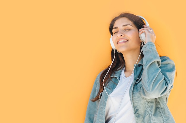 relaxed woman listening music against yellow background